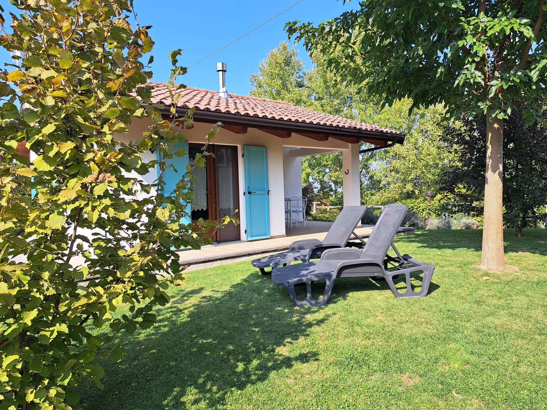 Il Ciabot di Rosa a Cherasco: la casa con portico, persiane azzurre, sdraio sul prato e noccioli in giardino